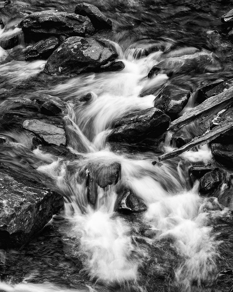 Dramatic black and white landscape photograph of whitewater rapids in a rocky canyon stream, with the water blurred by long-exposure.