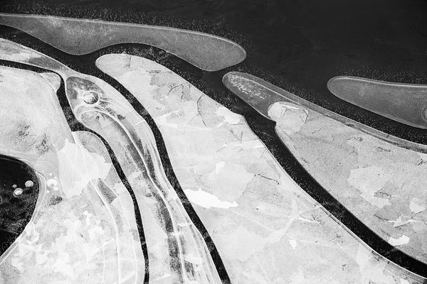 Black and white landscape photograph, abstract composition pond ice formed along the shoreline. A natural abstraction formed by organic shapes.