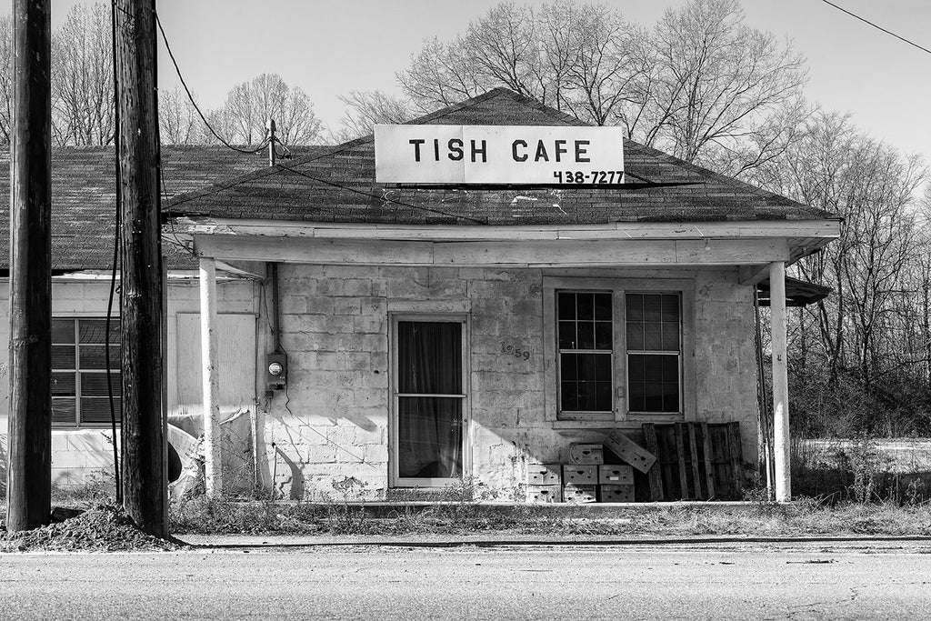 Black and white photograph of abandoned cafe with cartons and pallets stacked on the front porch in Tishomingo, Mississippi.