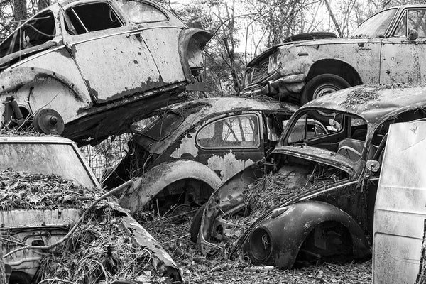 Black and white photograph of VW Beetles and other cars piled up in a discontinued junkyard.