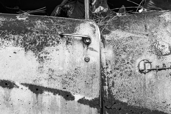 Black and white fine art detail photograph of the rusty driver's side door on a classic American car, junked and abandoned in the forest.