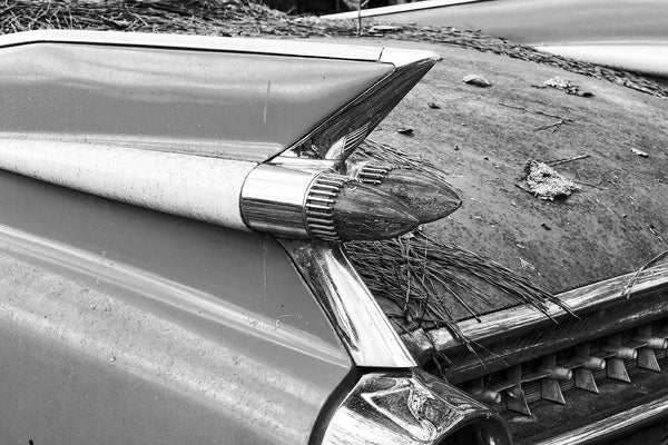 Black and white fine art photograph of a design detail — the rocket-style tail fin and tail lamps — on a rusting, abandoned classic American car.