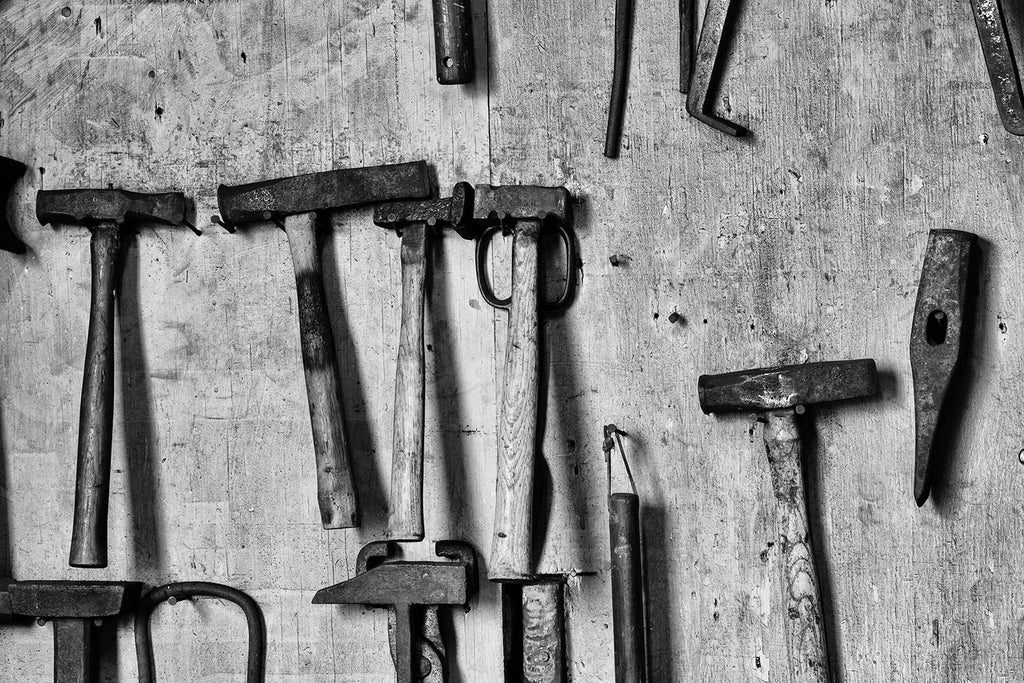 Black and white fine art photograph of tools hanging on the wall of a working blacksmith shop.
