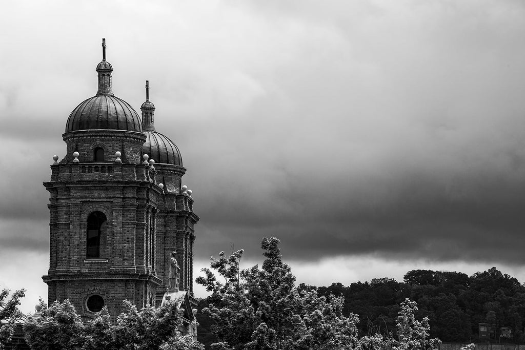 Black and white photograph of dark storm clouds over the hills of Asheville, North Carolina, featuring the twin towers of the Basilica of St. Lawrence on the left.