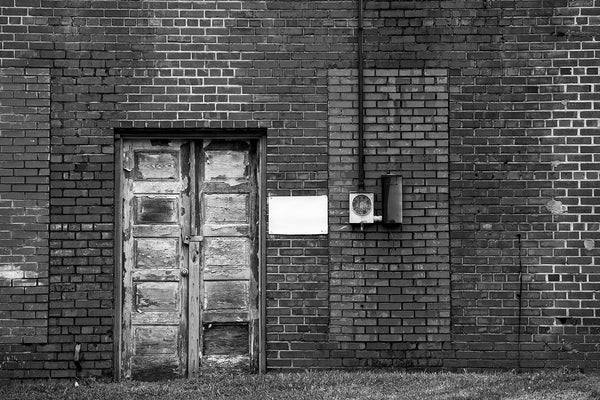 Black and white photograph of an abandoned building—the back side of an old storefront—in a small town in North Carolina. The cracked wooden doors, varying brick patterns, and repeated rectangle motif make this composition interesting.