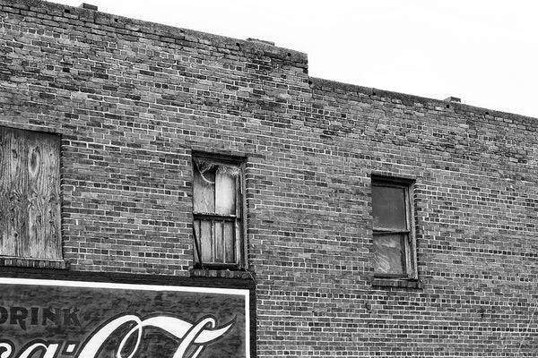 Black and white architectural detail photograph of broken windows and part of an old Cola-Cola wall ad seen in Gastonia, North Carolina.