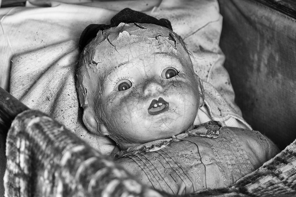 Black and white photograph of a beautifully cracked and dusty antique doll with a somewhat frightening look on its face.