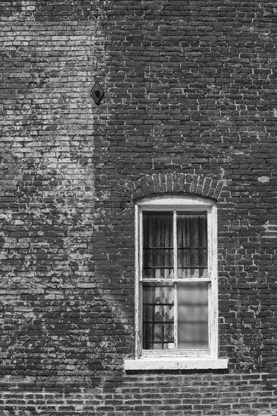 Black and white architectural detail photograph of lace curtains in the window of a historic brick building in picturesque Ste. Genevieve, Missouri.