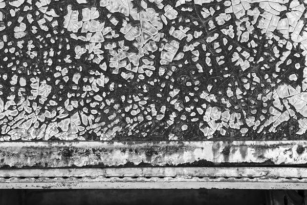 Black and white abstract photograph of chipped and peeling paint on the rusty metal exterior of an abandoned vintage railroad dining car.