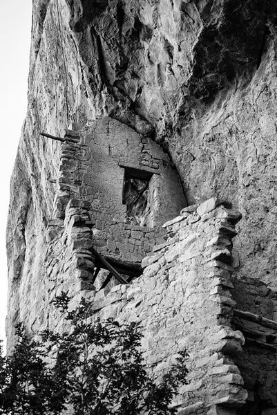 Black and white fine art photograph looking up at ancient walls built into the mesa wall at Mesa Verde, Colorado.