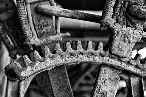 Black and white photograph of the gear mechanism of an antique farm tractor, which is still caked with the dried mud of the fields where it once worked.