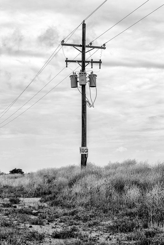 Black and white photograph of a telephone pole in the Texas Panhandle with a small sign that says, "BIG."
