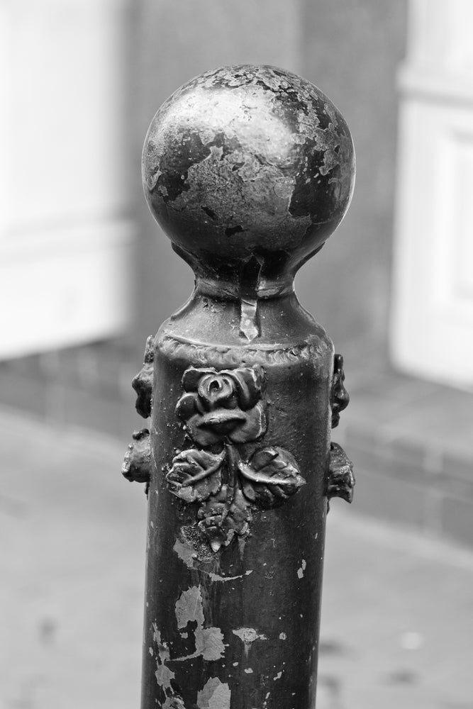 Black and white photograph of a black metallic post in the French Quarter of New Orleans, adorned with small black roses.