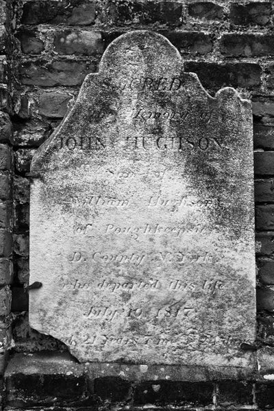 Black and white photograph of a broken old headstone in Savannah's historic Colonial Cemetery. Established in 1750, the burial ground expanded to six acres and was closed to interments in 1853. It now serves as a public park in Savannah's historic district.