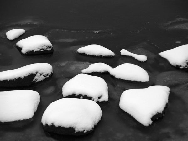 Black and white photograph of snow-covered rocks in the cold, black Charles River near Harvard in Cambridge, Massachusetts.