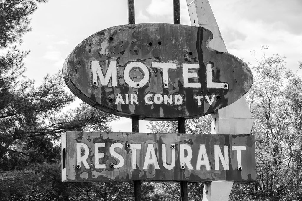 Black and white photograph of a fading, vintage Motel sign that has been repainted, increasing the texture and patina of its surface. The sign says "Motel - Air Cond - TV - Restaurant."