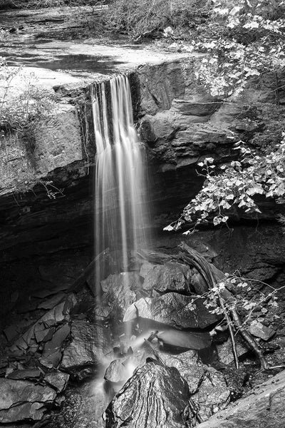 Black and white landscape photograph of a beautiful waterfall, with just a trickle of a stream that forms a soft thin veil as it goes over the edge of the stone cliff.