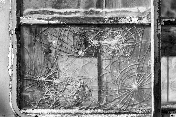 Black and white photograph of patterns in cracked window glass on a rusty old abandoned passenger train car.