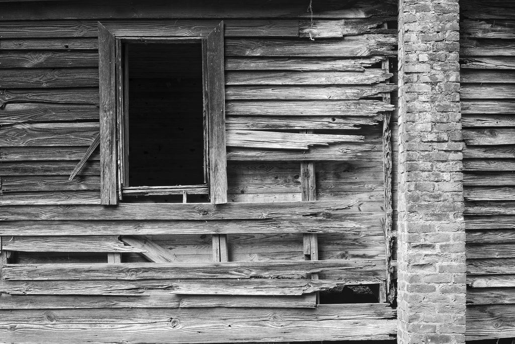 Black and white photograph of the weathered and broken wood and brick remnants of an abandoned old house. This photograph is a study in proportions and textures.