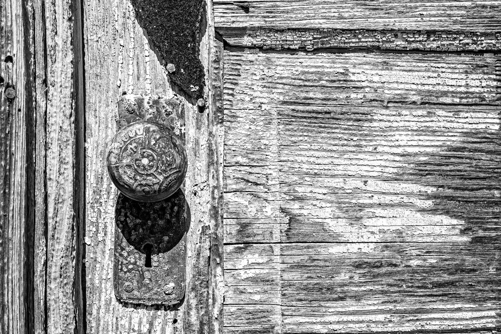 Black and white detail photograph of a weathered wooden door with a rusty ornate antique door knob seen in the Mississippi Delta.