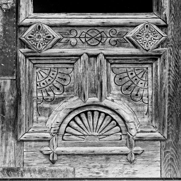 Black and white fine art photograph of a weathered old wooden door with fancy design patterns. (Square format)