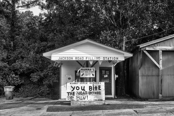 Black and white photograph of an old filling station turned into a hamburger and hot dog stand in Vicksburg, Mississippi. The hand-painted sign in front reads, "You bite the meat before the bun!"