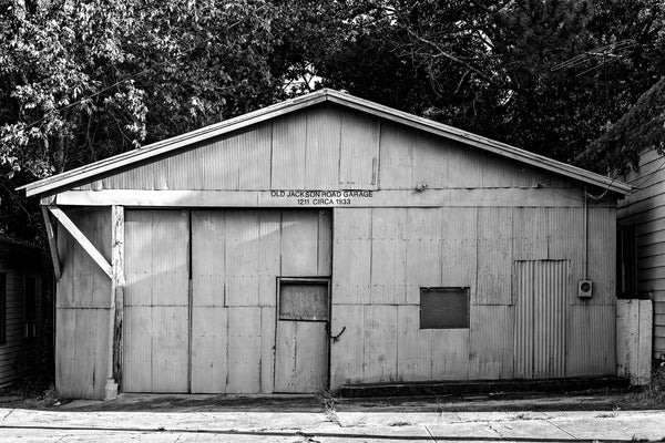 Black and white photograph of an old garage building with a sign that says "Old Jackson Road Garage, Circa 1933." 
