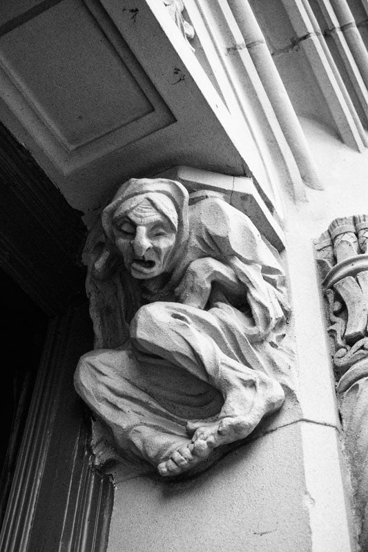 Black and white fine art architectural photograph of a wretched gargoyle figure in the street level doorway of The Emily Morgan Hotel in San Antonio, Texas. 
