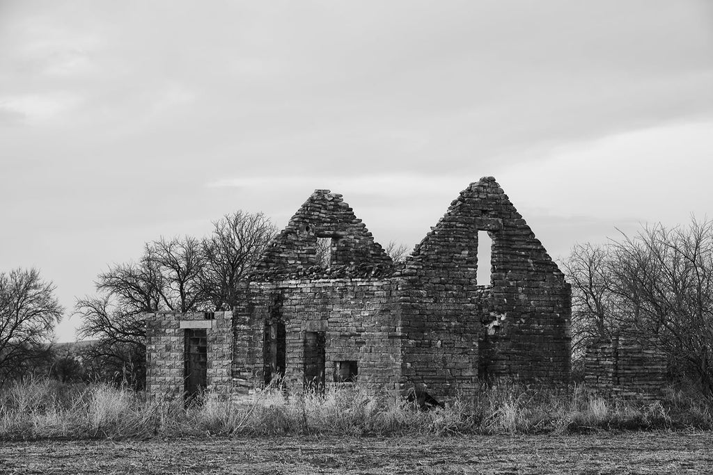 Black and white fine art photograph of an abandoned and collapsing stone farmhouse on the American prairie. 