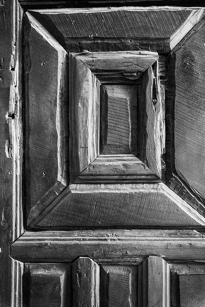 Black and white photograph of one of the rustic hand-carved wooden chapel doors at Mission San Jose in San Antonio, Texas.