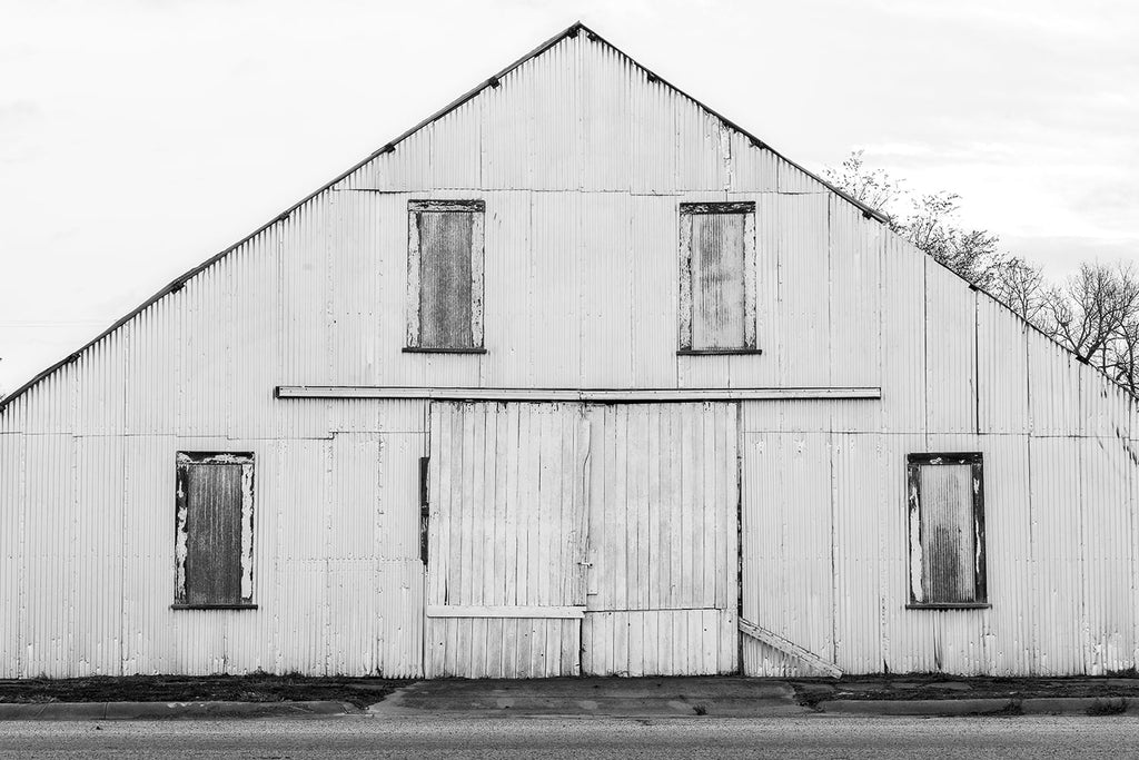 Black and white fine art photograph of an old shed painted white, with it's steep roofline forming a strong triangular composition with rectangles and lines.