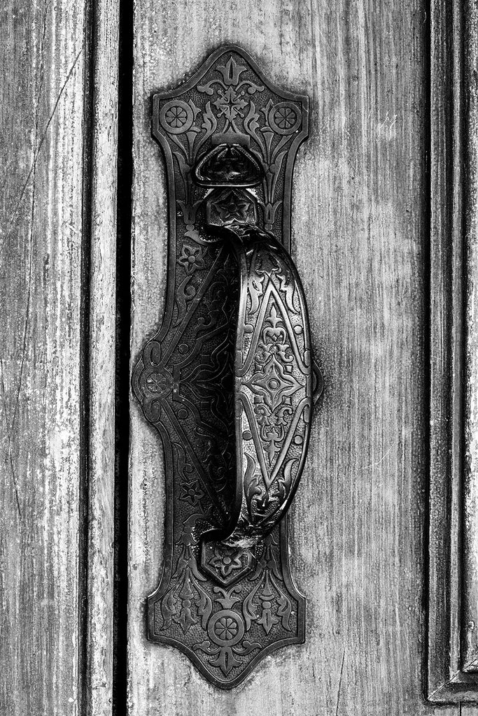 Black and white architectural detail photograph of an ornately detailed old door pull on the door of an 1880s-era library building.