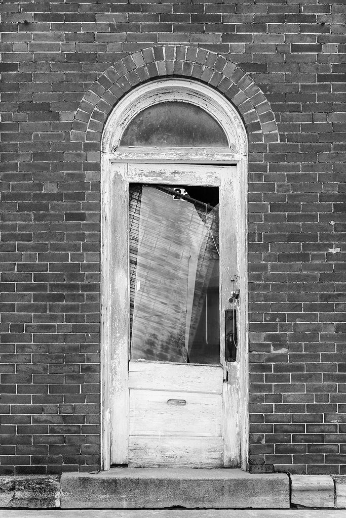 Black and white fine art photograph of an an old wooden door with a fanlight window in an abandoned storefront building in a small Midwestern town.