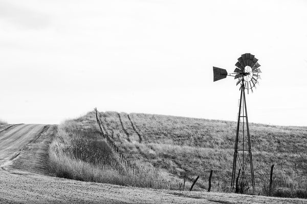 Black and white fine art photograph of the American prairie landscape featuring a dirt road and a windmill.