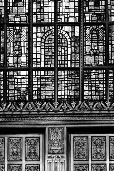 Black and white photograph of the old Alamo National Bank building built 1929 in San Antonio, Texas. This architectural detail photograph focuses on a section of the famous, massive stained glass window depiction of the Alamo, and some of the ornate metallic embellishment on the exterior of the building, which is now a hotel.