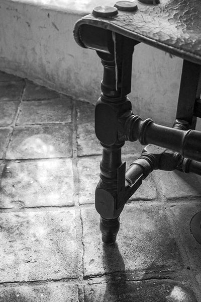 Black and white photograph of an antique Spanish chair on an old tile floor in the Spanish Governor's Palace in San Antonio, Texas.