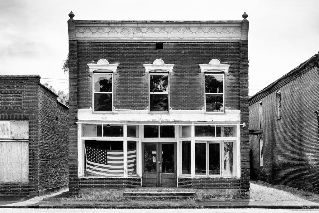 Black and white photograph of the front of an abandoned commercial building on the old Main Street in the ghost town of Pamplin City, Virginia. The street is lined with 11 historic and deserted buildings.