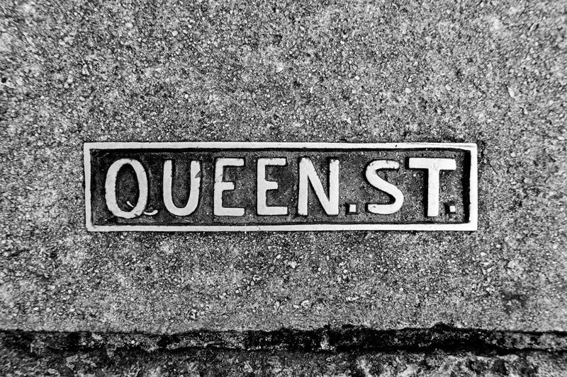 Black and white photograph of a Queen Street sidewalk sign placard in historic Charleston. 