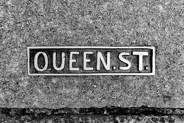 Black and white photograph of a Queen Street sidewalk sign placard in historic Charleston. 