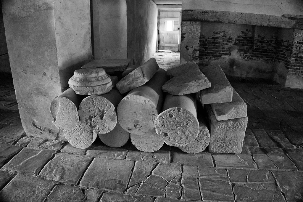 Black and white photograph of old stone columns stacked in the basement of Drayton Hall since at least the 1870s. Someone had them stacked there for storage, and they were never retrieved. Drayton Hall, built in the English Palladian style in 1738 near the bank of the Ashley River, was a grand country home for the wealthy Drayton family.