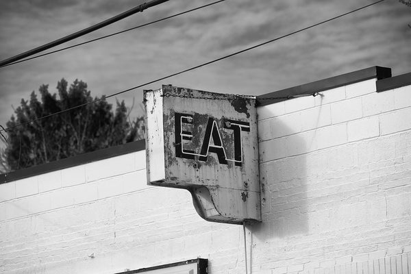 Black and white photograph of a rusty vintage neon diner sign that says "EAT" in capital letters.