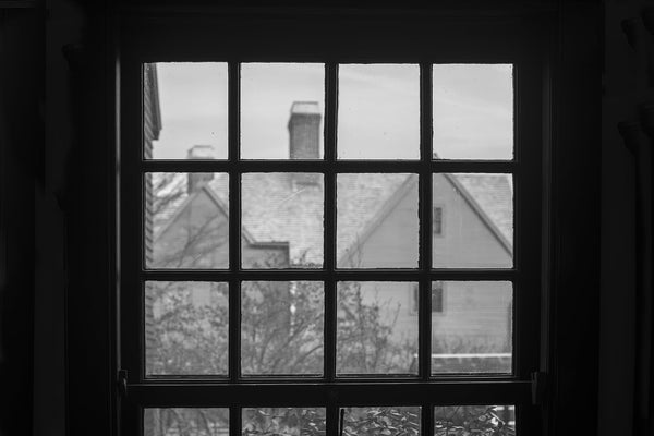 Black and white photograph of the historic "House of Seven Gables" as seen through the window of the Hawthorne house. Both iconic New England mansions are hundreds of years old.