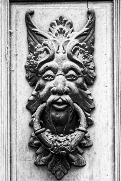 Black and white architectural detail photograph of an elaborate nature spirit door knocker on the door of an old building.