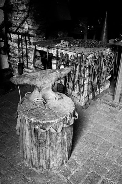 Black and white photograph of an anvil and tools in a blacksmith shop.