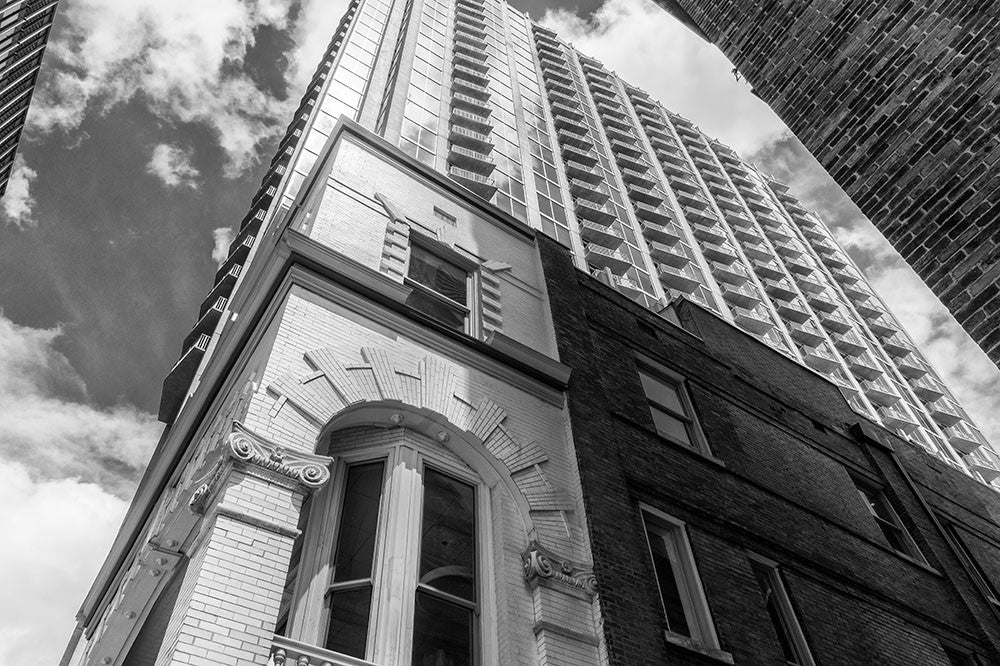 Black and white photograph looking up Nashville's historic Cohen building, dwarfed by modern skyscrapers, against a sunny Spring sky.
