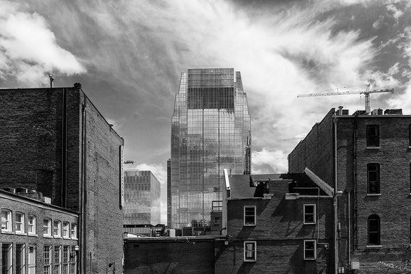 Black and white photograph of downtown Nashville featuring the Pinnacle Building, a modern glass office tower, framed by some of Nashville's older brick buildings and a few construction cranes.