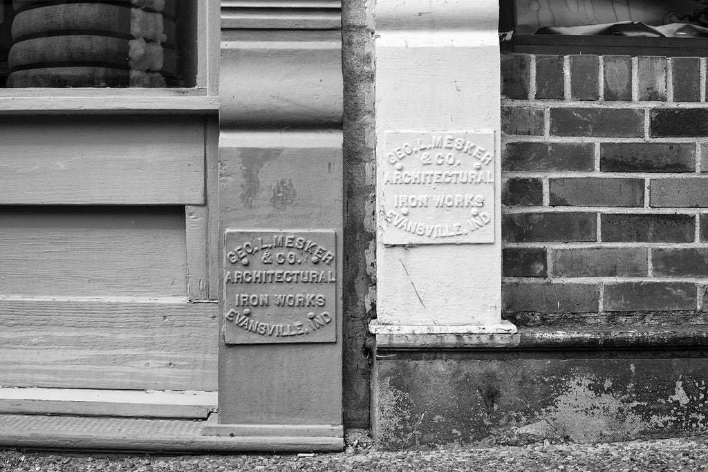Black and white architectural detail photograph of two Mesker Iron Works identification panels found on historic storefront buildings in a small town.
