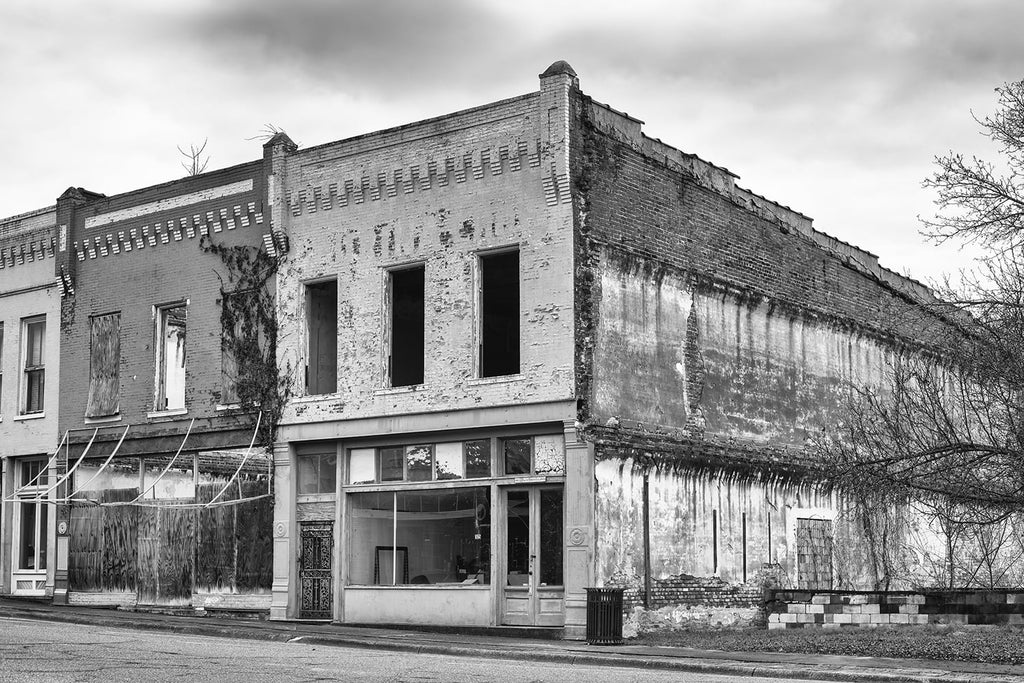 Black and white photograph of a block of historic but abandoned and derelict storefronts in a small town.