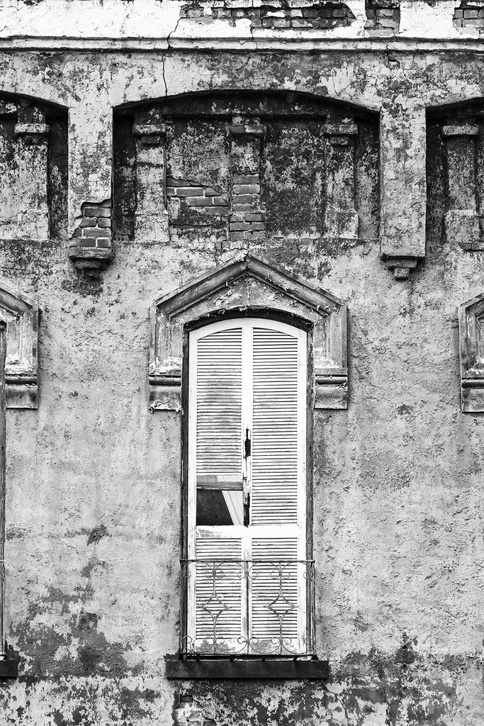 Black and white photograph of closed window shutters on an abandoned building with peeling paint and chipped bricks.