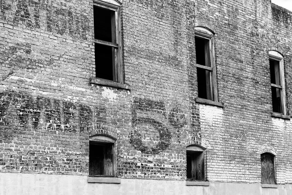 Black and white architectural detail photograph of the brick side of an abandoned building in a small town with a large fading wall ad advertising a price of 5 cents